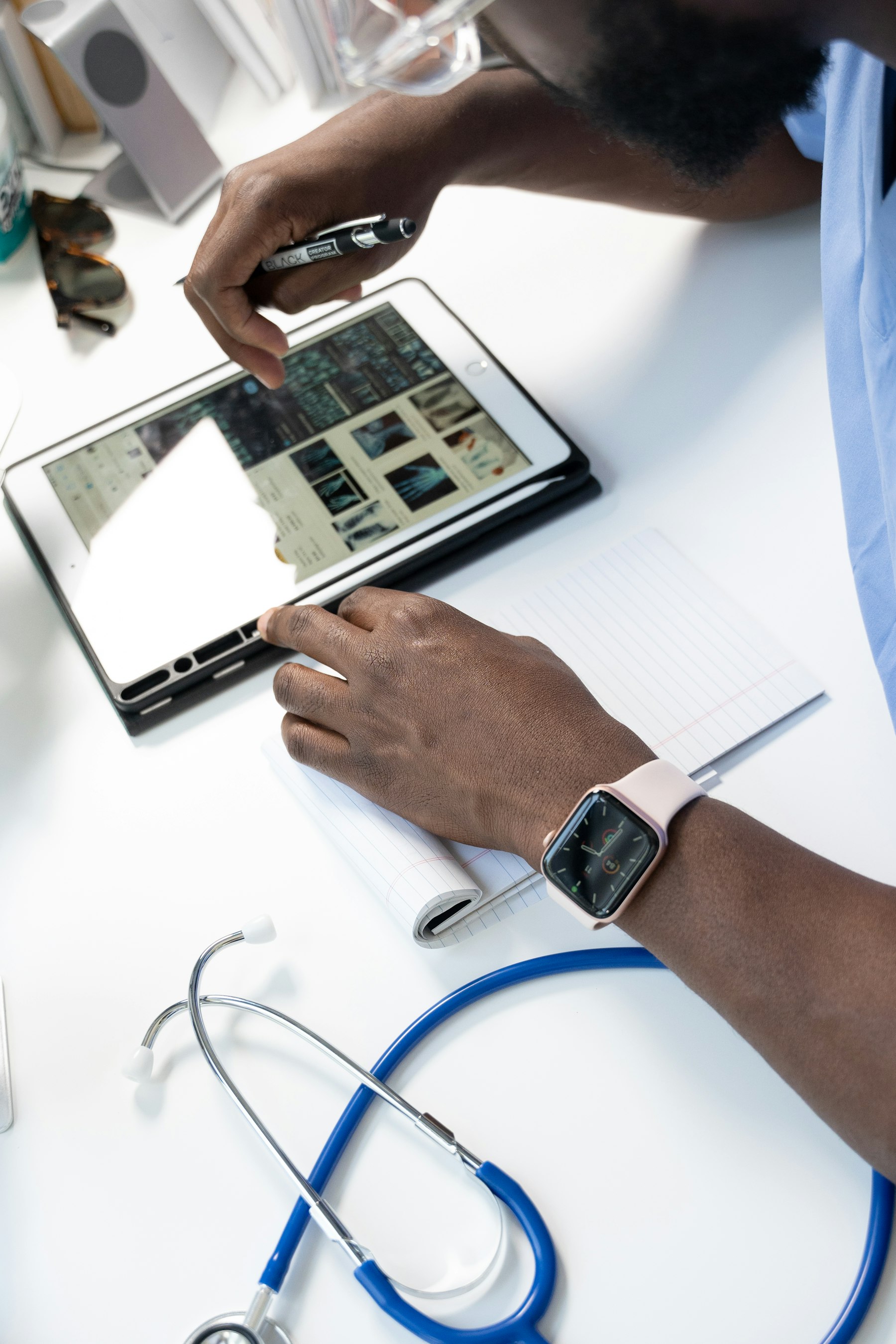 A clinician in scrubs reviewing X-rays on a tablet, stethoscope on the desk